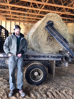 Hunter stands in front of a round bale on a trailer